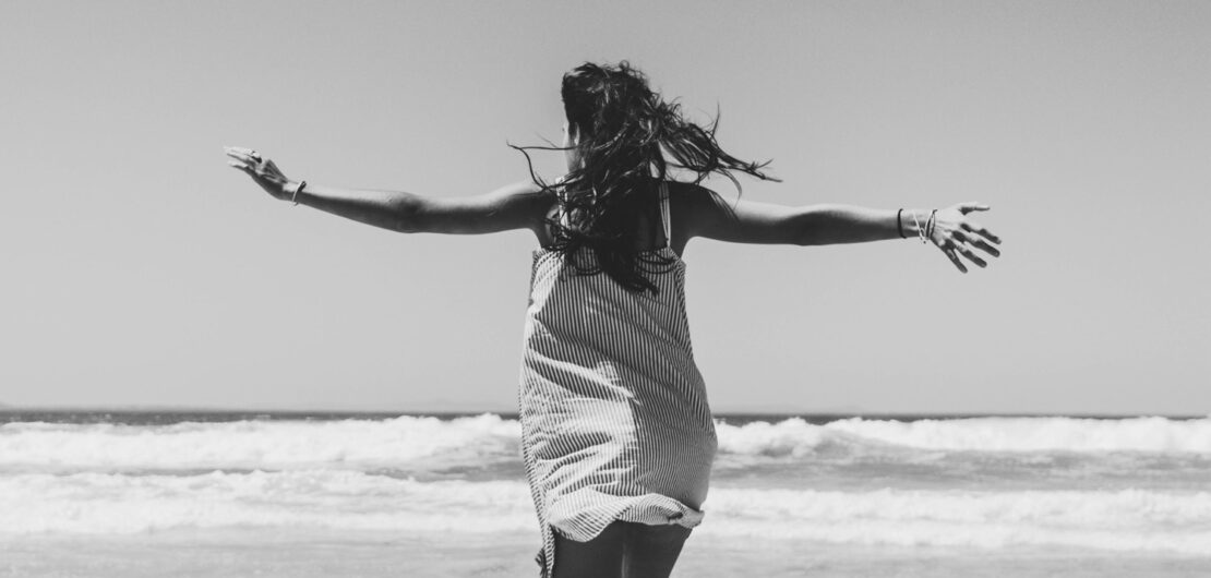 Woman with open arms facing the beach change your beliefs and change your life Leben ändern