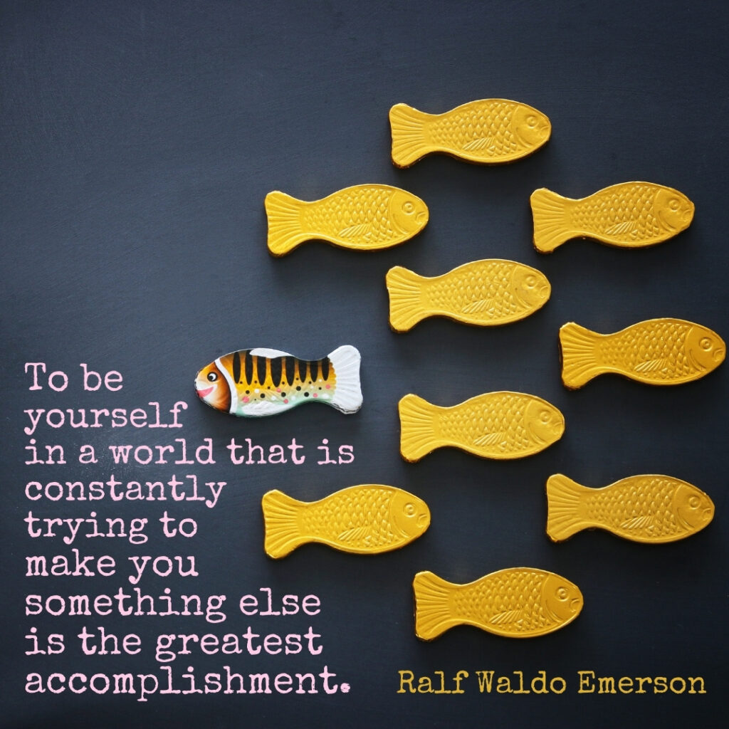 Picture of shoal of fish, one fish swimming in the other direction, Quote by Ralf Waldo Emerson: To be yourself in a world that is constantly trying to make you something else is the greatest accomplishment.